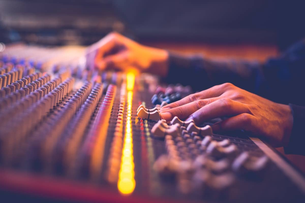 male producer, sound engineer hands working on audio mixing console in broadcasting, recording studio